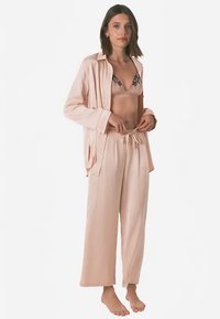 Nattøjssæt bestående af en lyserød skjorte med knapper og matchende løse bukser med snøre. Underneath en beige bh med sort blonder.