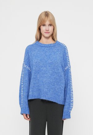 Sweater azul de malha com decote redondo, ombros caídos e detalhe de ponto branco ao longo das mangas. Tecido suave e texturizado.