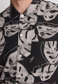 Schwarzes Kurzarmhemd mit weißem Blattmuster, Knopfkraagen, Tasche auf der linken Brust und strukturiertem Stoffdesign.