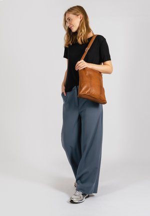 Brown leather shoulder bag with a single strap, paired with a black T-shirt and loose, wide-legged, light blue pants.