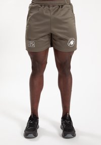 Olijfgroene sportieve shorts met een elastische tailleband. Heeft een wit grafisch logo en "82" bedrukt op de linkerdij. Textuurstof.