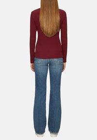 Burgundrotes Langarmtop, kombiniert mit hellblauen Schlagjeans. Der Stoff wirkt glatt und die Jeans haben eine klassische Denim-Textur.
