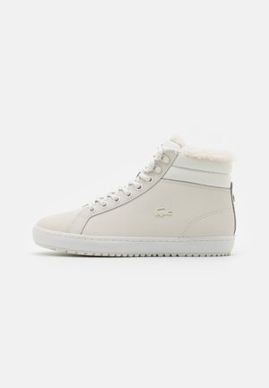 Zapatilla blanca de caña alta con forro de piel, cordones delanteros, suela de goma y logo de cocodrilo en el lateral, mostrada de perfil sobre un fondo liso.