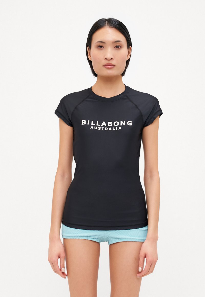 Μαύρο κοντομάνικο rash guard με λογότυπο "BILLABONG AUSTRALIA" σε λευκό. Απαλή ύφανση, εφαρμοστή γραμμή, σε συνδυασμό με ανοιχτό μπλε μαγιό.