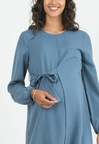 Umstandsjacke aus weichem, hellblauem Stoff, mit langen Ärmeln, einem Taillenzugdetail und einer sanften A-Linie für optimalen Komfort.