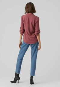 Camicia bordeaux con maniche arrotolate, abbinata a jeans a gamba dritta blu chiaro e stivali neri con tacco alto. Tessuto morbido, design semplice.