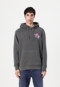 Sweatshirt cinzento com capuz e um bolso frontal, apresentando um gráfico colorido "TOMMY". Feito de tecido macio com punhos e bainha canelados.