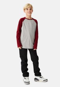 Grå langærmet skjorte med burgunder raglanærmer, kombineret med sorte jeans og hvide sneakers med sorte detaljer.