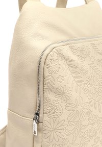 Mochila de cuero color crema con patrón floral en relieve, cremallera plateada y superficie texturizada. Laterales lisos y correas ergonómicas.