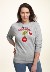Sweatshirt gris arborant un graphique coloré "Joyeux Grinchmas !" Le design présente une main verte tenant un ornement rouge, avec une coupe confortable.