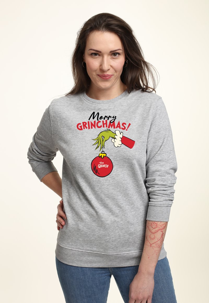 Sweatshirt gris arborant un graphique coloré "Joyeux Grinchmas !" Le design présente une main verte tenant un ornement rouge, avec une coupe confortable.