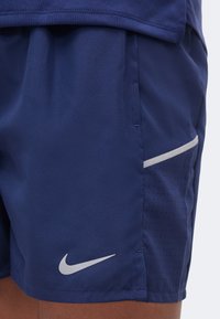 Μπλε ναυτικό σορτς με λευκό λογότυπο Nike στο τελείωμα, με ομαλό μπροστινό ύφασμα και διάτρητη πλαϊνή επιφάνεια με λευκό περίγραμμα.