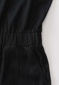 Czarna teksturowana tkanina z elastycznym pasem i detalem bocznej kieszeni na ubraniu.