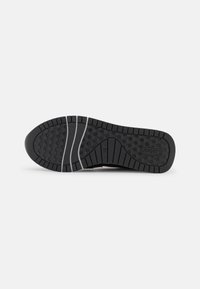 Suola di sneaker nera con superficie in gomma testurizzata; presenta scanalature orizzontali e motivi esagonali per aderenza e trazione.
