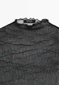 Černý průhledný top s texturovaným vzorem, s volánkovým výstřihem a jemnými lineárními motivy. Na štítku je napsáno "Massimo Dutti, Vyrobeno v Portugalsku."