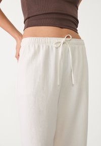 Bílé kalhoty volného střihu s elastickým pasem a šňůrkou na stažení. Vyrobené z lehkého materiálu, s hladkým povrchem a bez vzorů.