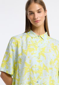 Korte mouwen shirt in lichtblauw met geel bloemenpatroon. Heeft een klassieke kraag, knoopsluiting aan de voorkant en een zachte stoftextuur.