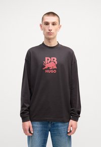 T-shirt a maniche lunghe grigio scuro in cotone, con un logo grafico rosa e la scritta "PB HUGO" sul davanti. Vestibilità casual con polsini a coste.