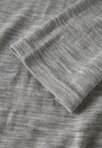 Siva pletenina s suptilnom heathered teksturom. Blizu prikazuje glatku površinu i uredno sašivene rubove. Mekani lagani materijal.