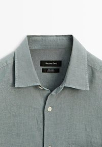 Jasnoszara lniana koszula z klasycznym kołnierzykiem, pięcioma guzikami i metką z napisem "Massimo Dutti". Teksturowana powierzchnia o naturalnym splocie.