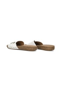 White slip-on sandals with a cork sole, featuring a wide strap, metal buckle, and decorative round studs along the edge.