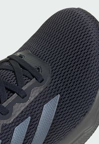 Zapatilla de running de malla negra con parte superior texturizada, acentos en franjas grises y cordones negros. Cuenta con una superposición sintética para mayor soporte.