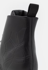 Bottine noire en cuir lisse, avec un motif embossé en forme de toile d'araignée sur le côté et un onglet de maintien pour un enfilage facile.
