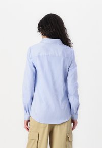 Chemise à manches longues rayée bleue et blanche avec col, dotée de poignets boutonnés et d'un ourlet arrondi. Fabriquée en tissu léger.