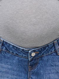 Gros plan sur la taille d’une personne portant un jean en denim bleu avec un bouton fermé et une chemise grise rentrée.