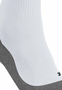 Calcetín deportivo blanco acanalado con suela acolchada gris y detalles en negro del logo. Textura suave, diseño de altura media y tejido transpirable.