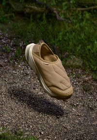 Pantofii slip-on bej prezintă un superior căptușit cu textură matlasată, o talpă ușoară și un branding discret pe laterală și călcâi.
