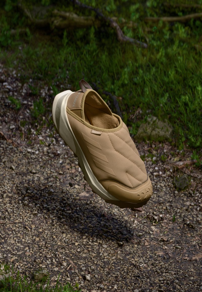 Sandalha bege de slip-on com um topo acolchoado e textura em matelassé, uma sola leve e uma marca discreta na lateral e no calcanhar.