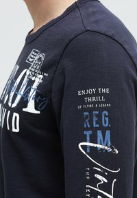 Navyblaues Langarmshirt mit Rundhalsausschnitt; verfügt über weiße und blaue grafische Texte auf der Vorderseite und dem Arm; weicher Baumwollmix; lässige Passform.