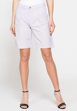 Donna che indossa pantaloncini lavanda chiaro al ginocchio con pieghe frontali e chiusura con bottone abbinati a sandali neri con tacco alto.