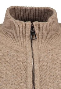 Beżowy sweter z dzianiny z wysokim kołnierzem, z metalowym zamkiem błyskawicznym z przodu. Struktura jest prążkowana z miękkim, tkanym wykończeniem.
