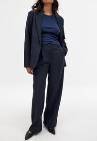 Námornícka blazer a prispôsobené nohavice, vyrobené z hladkej tkaniny, s klasickým strihom. Nosené s rebrovaným námorníckym topom a špicatými čiernymi topánkami.