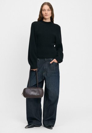 Maglione nero a maglia con maniche lunghe, abbinato a jeans di denim scuri e larghi e una borsa in pelle marrone con chiusura a zip.