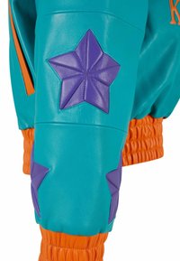 Tyrkysová kožená bunda s fialovými hvězdičkovými nášivkami, oranžovými žebrovanými manžetami a bočními detaily. Hladká textura s výraznými barevnými kontrasty.