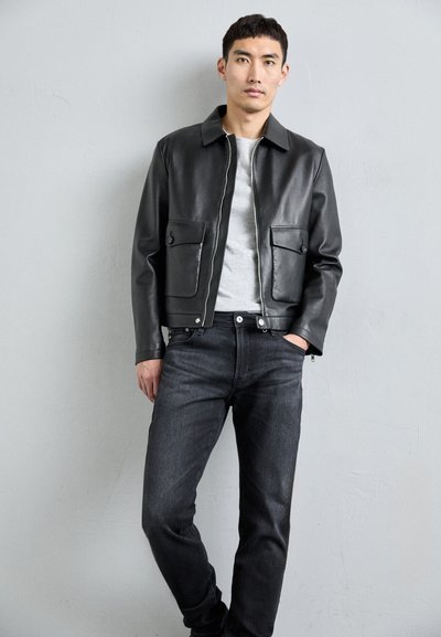 Svart läderjacka med dragkedja fram, två bröstfickor och krage. Bärs över en grå skjorta och matchas med mörka jeans.