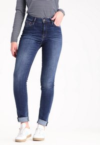 Smala jeans i mörkblått denim med hög midja, knappstängning och rullade cuffs. Kombinerad med vita sneakers och en svart-vit randig topp.