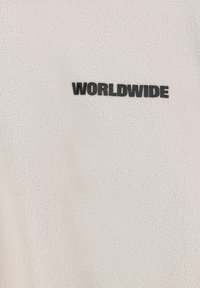Fleece sweatshirt in light beige with a soft texture, featuring the word "WORLDWIDE" in bold black lettering on the front.