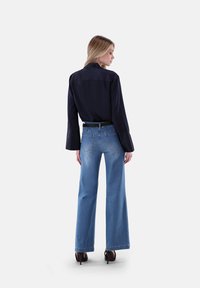Blusa blu navy con maniche lunghe e yoke posteriore, abbinata a jeans a gamba larga di un delicato blu chiaro, dotati di un classico design a cinque tasche e una cintura nera.