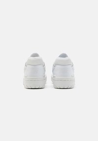 Weiße Sneaker mit einem glatten Leder-Obermaterial, strukturierten Akzenten, einem gepolsterten Kragen und einer verstärkten Gummisohle mit Traktionsmuster.