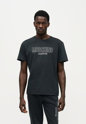 Un mannequin masculin porte un T-shirt noir Moschino Active et un pantalon assorti sur un fond clair et uni.