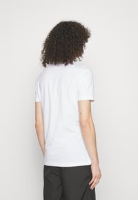 White short-sleeve t-shirt made of cotton, featuring a classic round neckline and a smooth, soft texture, worn with dark shorts.