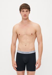 Črne bokserice z sivo elastično obrobo, ki nosi logotip Nike. Material se zdi gladek in prilegajoč, s srednje dolgim dizajnom.