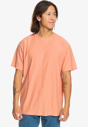 Short-sleeve t-shirt in coral orange, made of a textured fabric. Features a small logo on the chest and a relaxed fit.