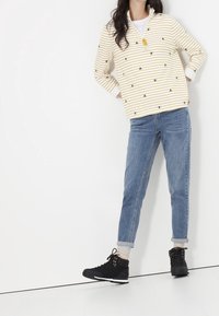 Suéter a rayas amarillo y blanco con bordados florales, combinado con jeans azul claro y botas negras con cordones y acentos dorados.