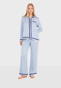 Light blue pajama set with a geometric pattern, featuring a button-up shirt and wide-leg pants with navy trim and accents. Soft fabric texture.