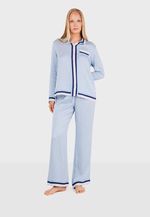 Lichtblauw pyjama set met een geometrisch patroon, bestaande uit een knoopsluiting shirt en wijde broek met marineblauwe rand en accenten. Zachte stofstructuur.